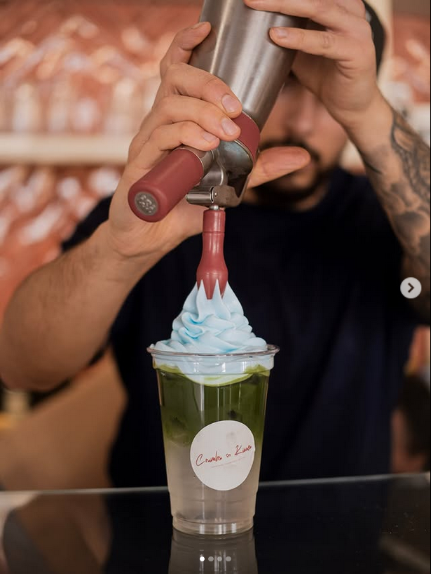 Barista bereitet einen geschichteten Matcha-Specialty-Drink mit sanftem Topping zu